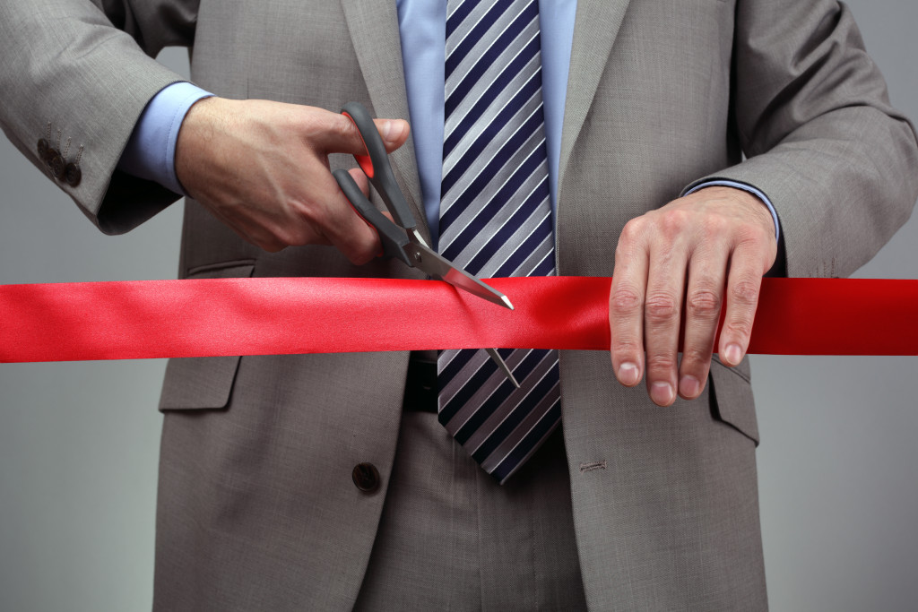 A business owner uses a large pair of scissors to cut a red ribbon